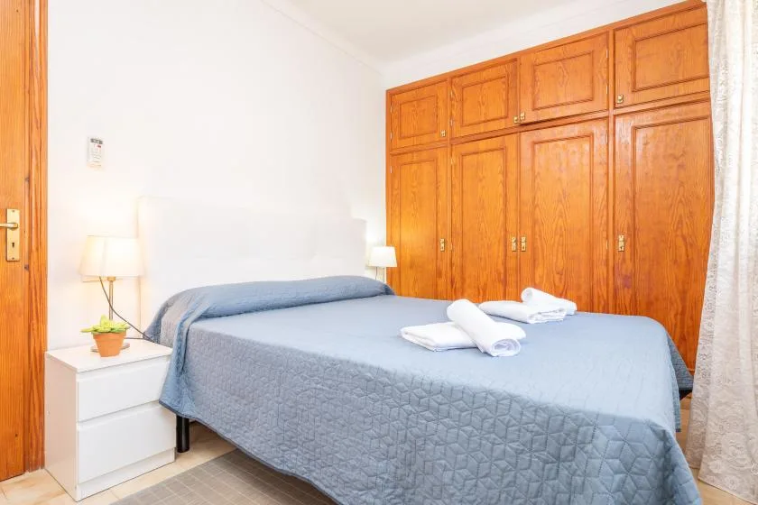 A bedroom with a bed dressed in blue bedding and wooden wardrobes.