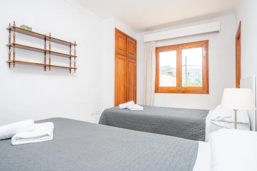 A bright bedroom with two beds and a wooden-framed window.