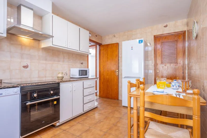 A tiled kitchen with white cabinets, appliances, and a wooden dining table.
