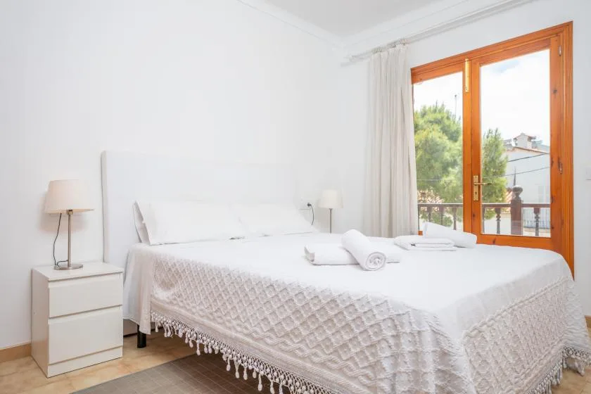 A bright bedroom with a white bed beside a large window.
