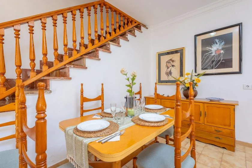 A dining area with a wooden table set beneath a staircase.