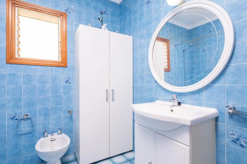 A blue-tiled bathroom with a sink, mirror, and white storage cabinet.