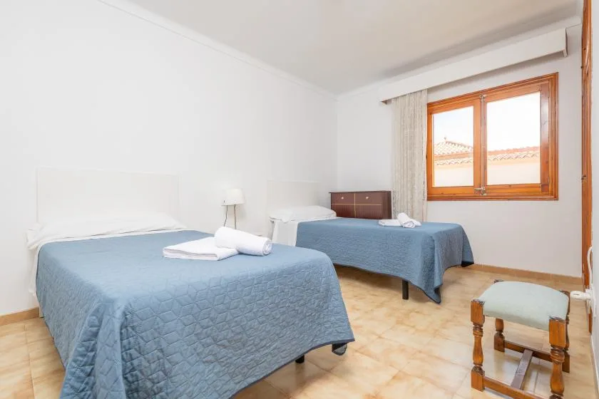 A bright bedroom with two beds dressed in blue bedspreads and a window.