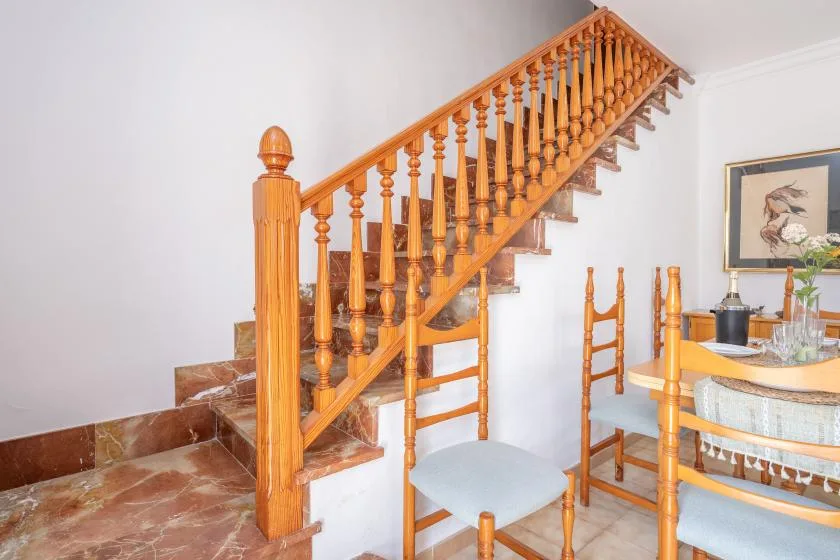 A wooden staircase rises beside a dining area with chairs and a table.