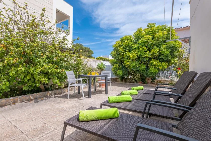 A sunny outdoor patio with lounge seating, a dining table, and leafy greenery.
