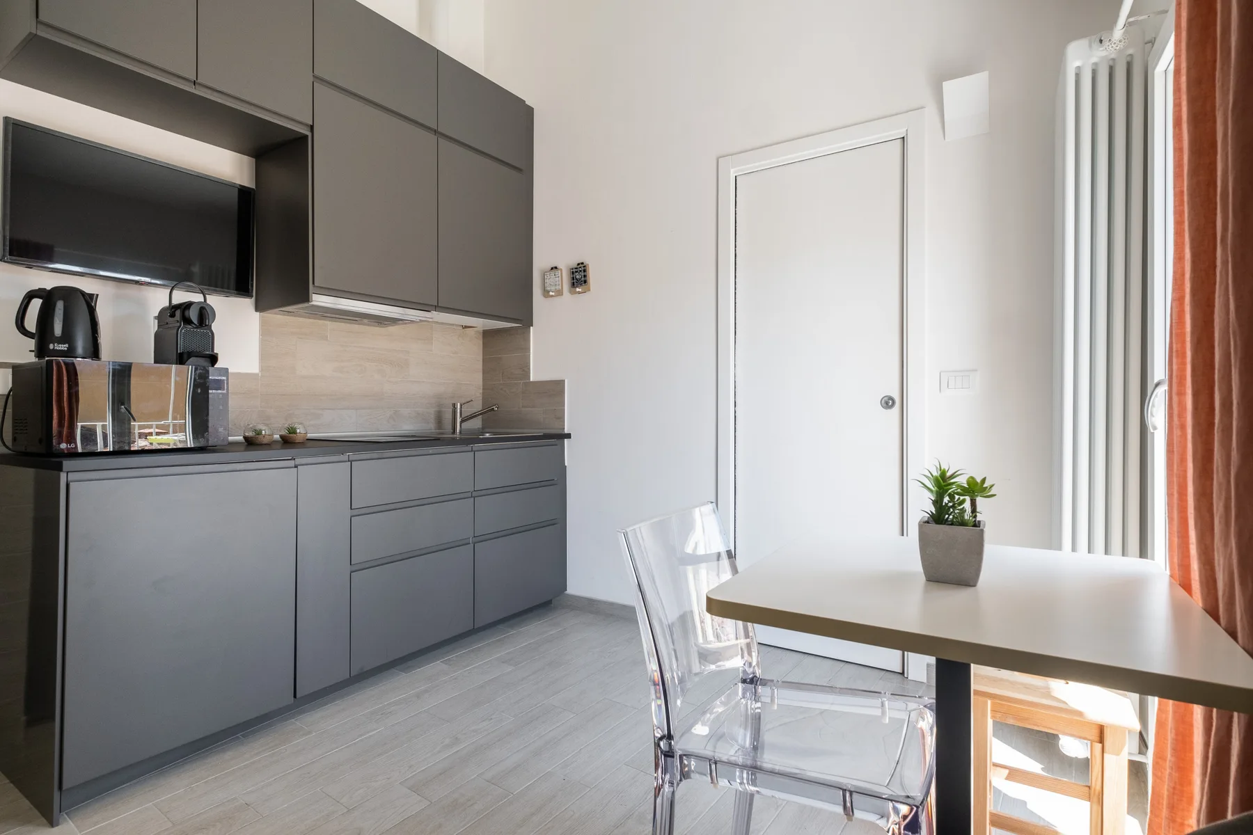 A compact kitchen and dining area with gray cabinets and a table by the window.