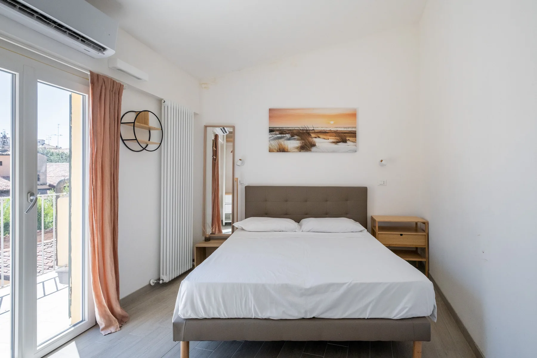 A bright bedroom with a bed, bedside tables, and a balcony door.