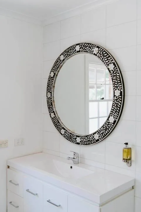Un tocador de baño luminoso con lavabo y un espejo ovalado ornamentado.