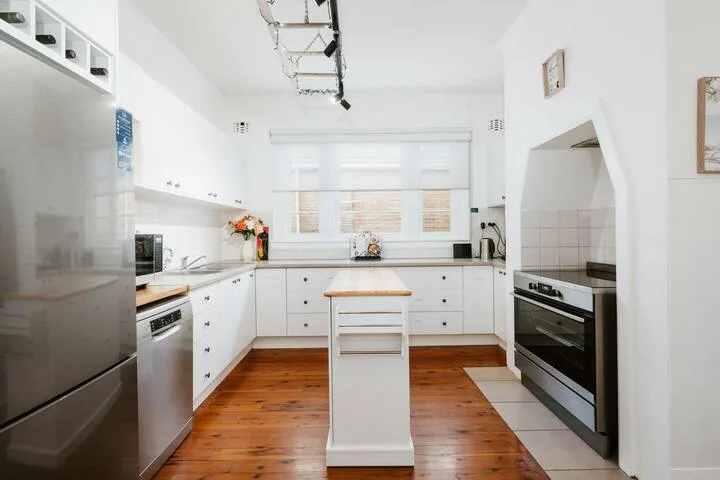 Una cocina luminosa con gabinetes blancos, electrodomésticos de acero inoxidable e isla central.