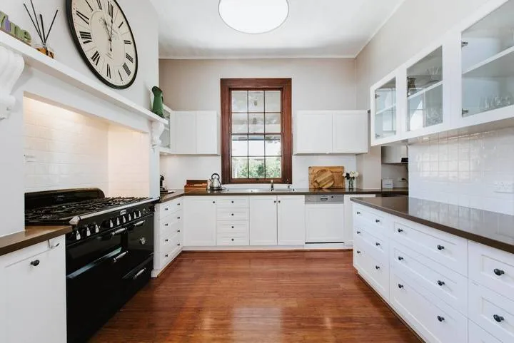 Una cocina luminosa con armarios blancos, encimeras oscuras y una ventana central.