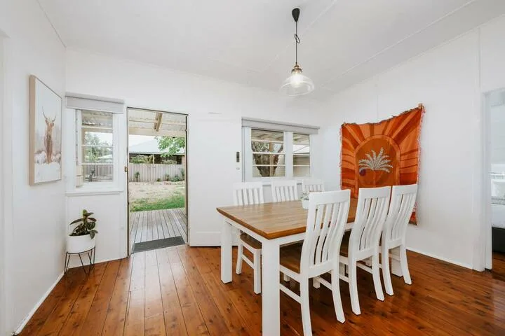 Un comedor luminoso con una mesa de madera y asientos blancos junto a una puerta de vidrio.
