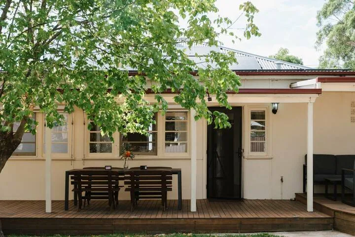 Un patio cubierto con asientos al aire libre está junto a una casa bajo ramas frondosas.