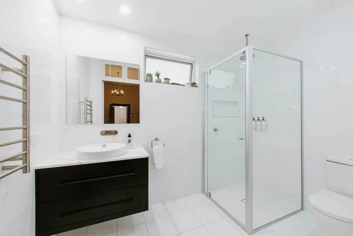 Un baño luminoso con lavabo, espejo y ducha de vidrio.