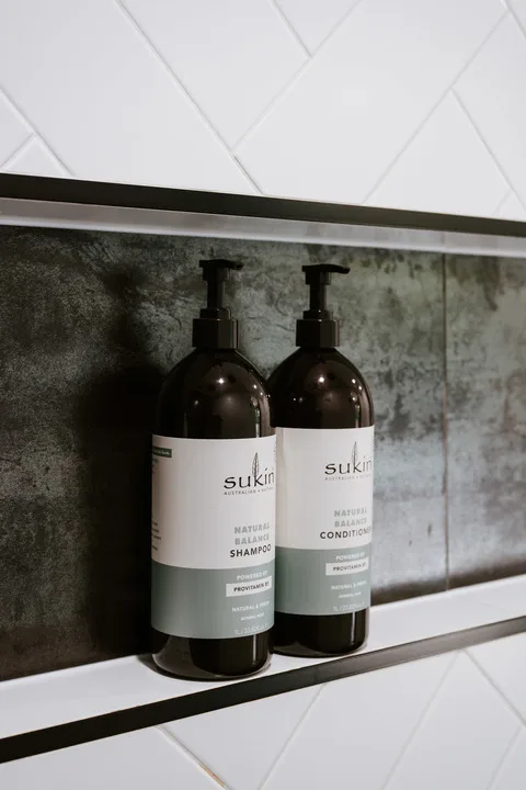 Un estante de baño muestra botellas de champú y acondicionador frente a paredes revestidas de azulejos.