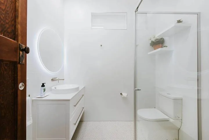 Un baño luminoso con lavabo, espejo iluminado y ducha con mampara de vidrio.