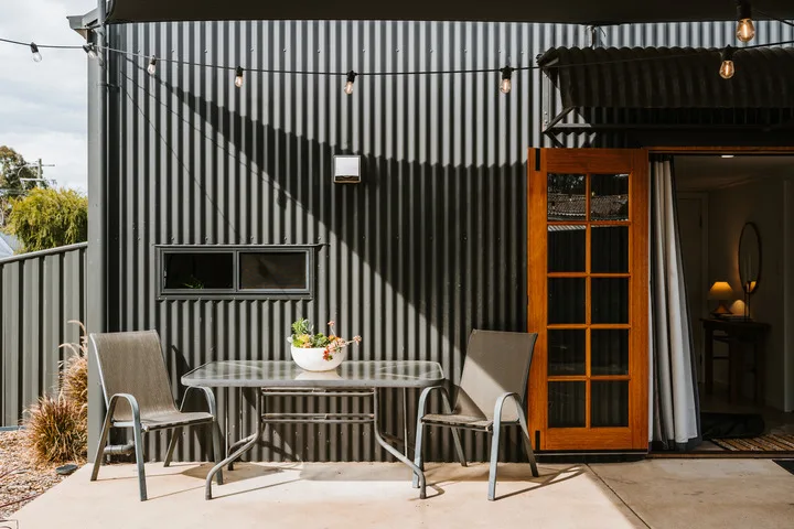 Una zona de estar en un patio con mesa y sillas junto a una pared exterior a rayas.