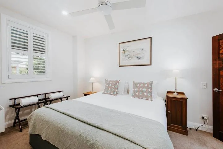 Un dormitorio luminoso con una cama, una ventana con persianas y mesitas de noche.
