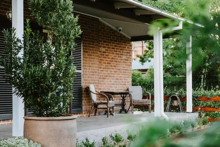 Un patio cubierto con asientos al aire libre junto a una pared de ladrillo y un jardín.