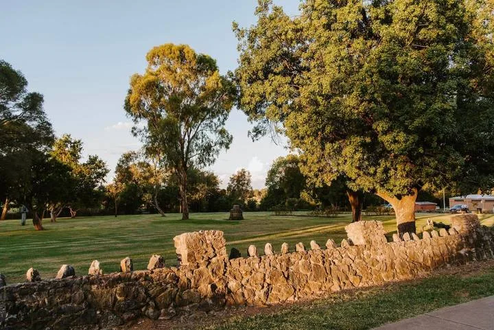 Un parque con césped, árboles frondosos y un muro bajo de piedra.