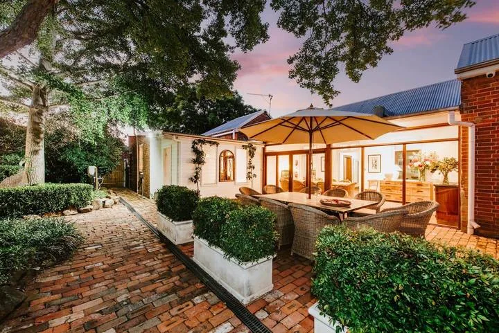 Un patio exterior con asientos bajo una sombrilla grande, junto a un camino de ladrillo.