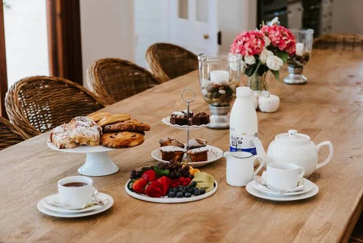Una mesa de comedor está preparada con pasteles, fruta, té y flores.
