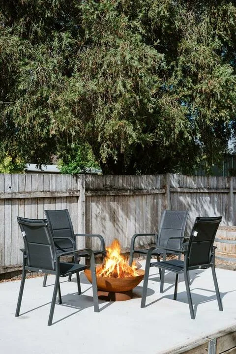 Un patio al aire libre con asientos alrededor de un brasero bajo un árbol grande.