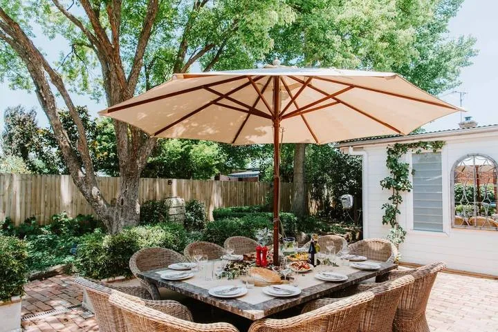 Una zona de comedor al aire libre está bajo una gran sombrilla en un jardín frondoso.