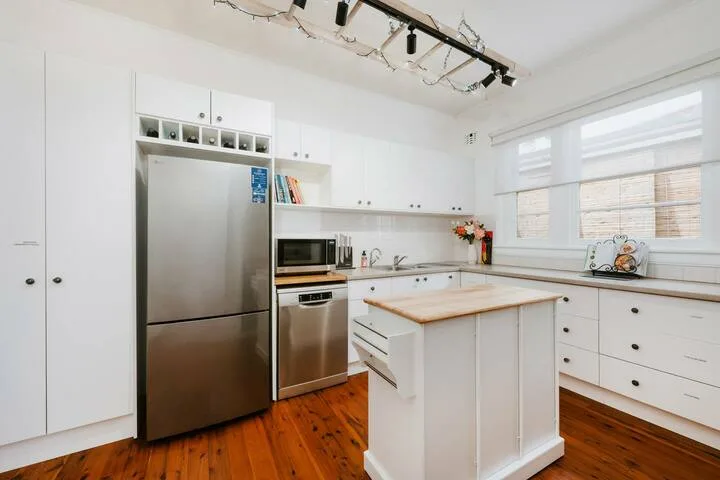 Una cocina blanca y luminosa con electrodomésticos de acero inoxidable y una isla central.