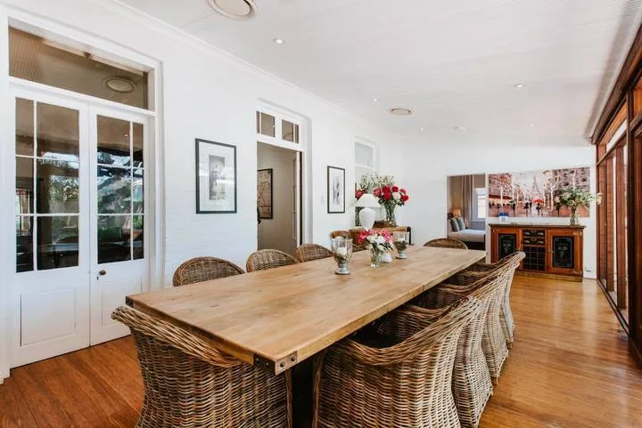 Un comedor cuenta con una larga mesa de madera, asientos tejidos y flores.