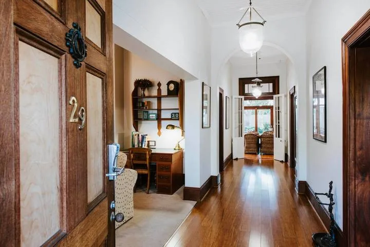 Un pasillo luminoso con suelo de madera conduce a una zona de estar y puertas abiertas.