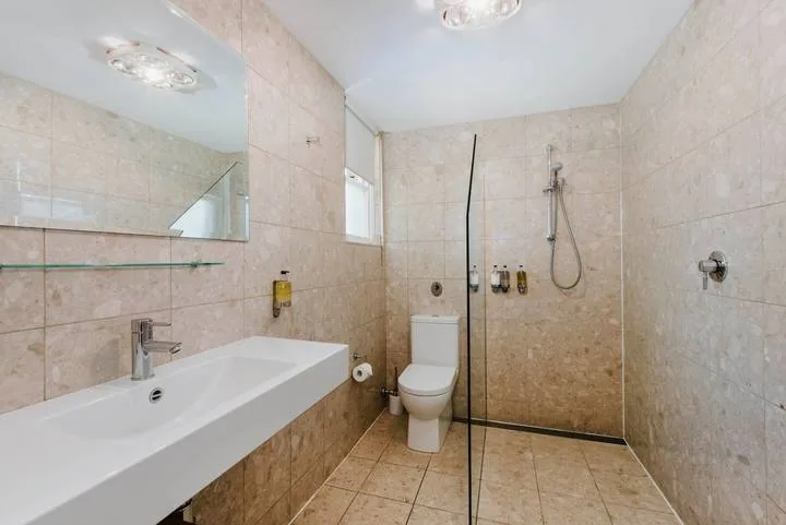 Un baño alicatado con lavabo, inodoro y ducha de pared.