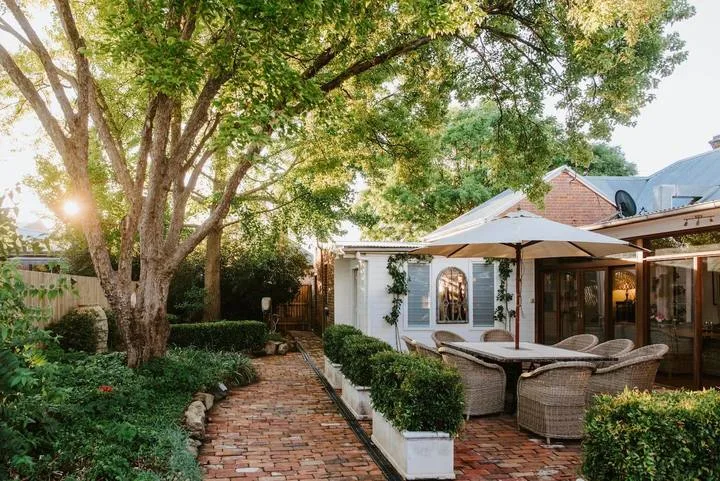 Un patio ajardinado de ladrillo con asientos al aire libre bajo un gran árbol frondoso.