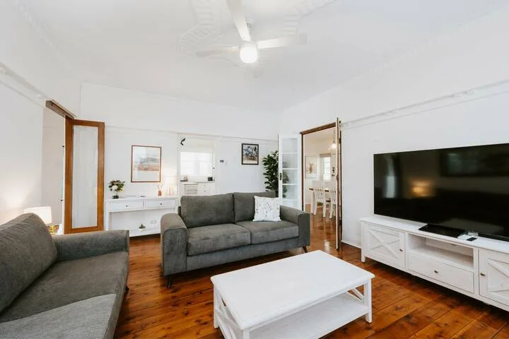Una sala luminosa con asientos grises, una mesa de centro blanca y un televisor.