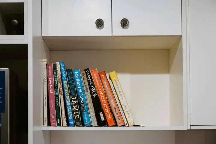 Una estantería empotrada tiene libros de colores bajo armarios blancos.