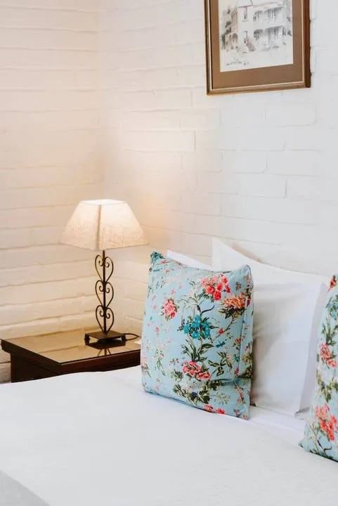 Una cama bien tendida con almohadas florales está junto a una lámpara encendida.