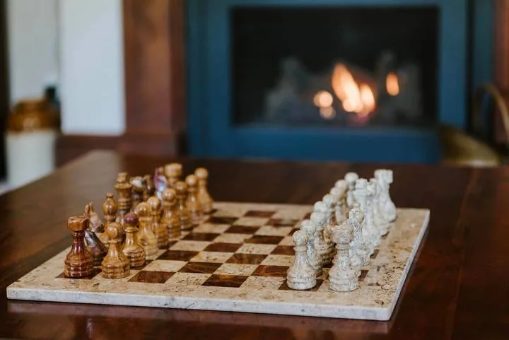 Un tablero de ajedrez con piezas de madera y blancas está sobre una mesa frente a una chimenea encendida.