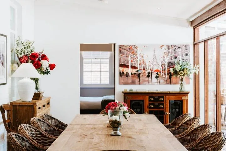 Comedor con una mesa de madera, asientos tejidos y un aparador.