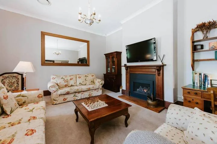 Una sala de estar con asientos florales, una mesa de centro de madera y un televisor sobre la chimenea.