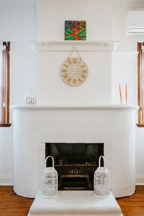 Una sala luminosa se centra en una chimenea blanca con un reloj redondo encima.