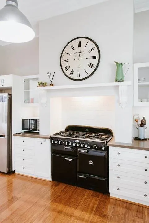 Una cocina luminosa con una estufa negra bajo un reloj grande.