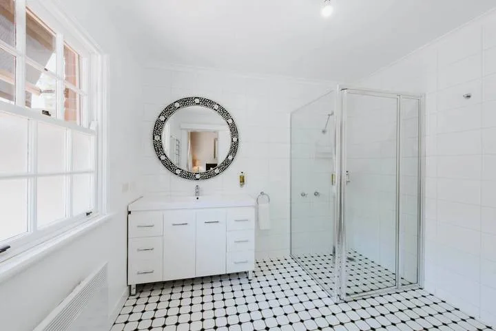 Un baño luminoso con lavabo, espejo redondo y ducha de vidrio.
