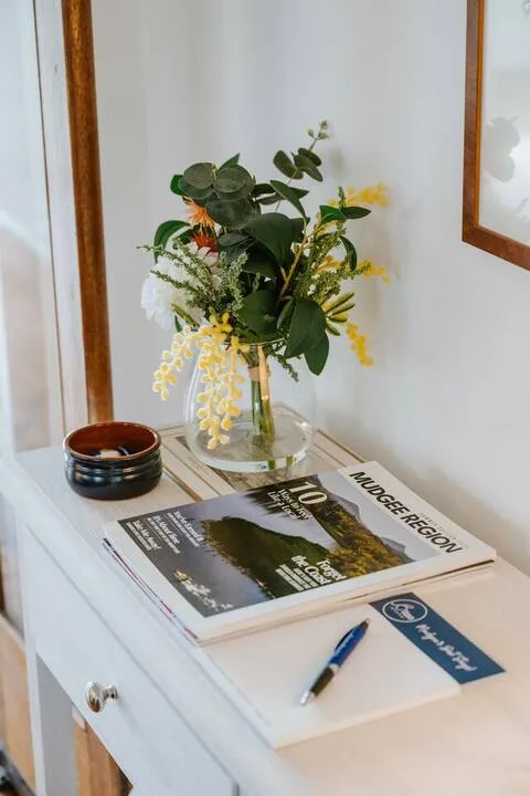 Una mesa consola muestra un arreglo floral, una revista regional y un bolígrafo.