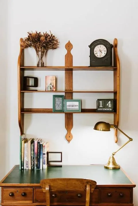 Un escritorio de madera con estantes exhibe libros, un reloj y una lámpara de latón.