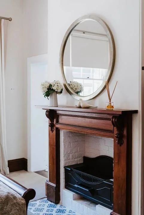 Una chimenea en una habitación, con un espejo ovalado grande y flores sobre la repisa.