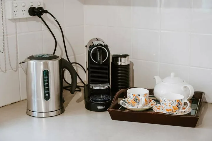 Una estación de té y café está sobre una encimera, con hervidor, cafetera, tazas y tetera.