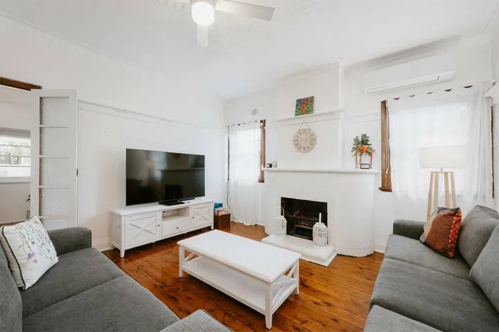 Una sala luminosa con asientos grises, un televisor y una mesa de centro blanca.