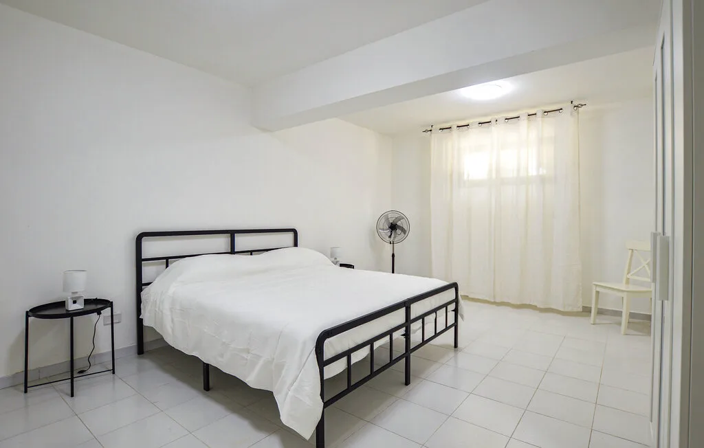 Un dormitorio luminoso con una cama, suelo de baldosas y cortinas translúcidas.