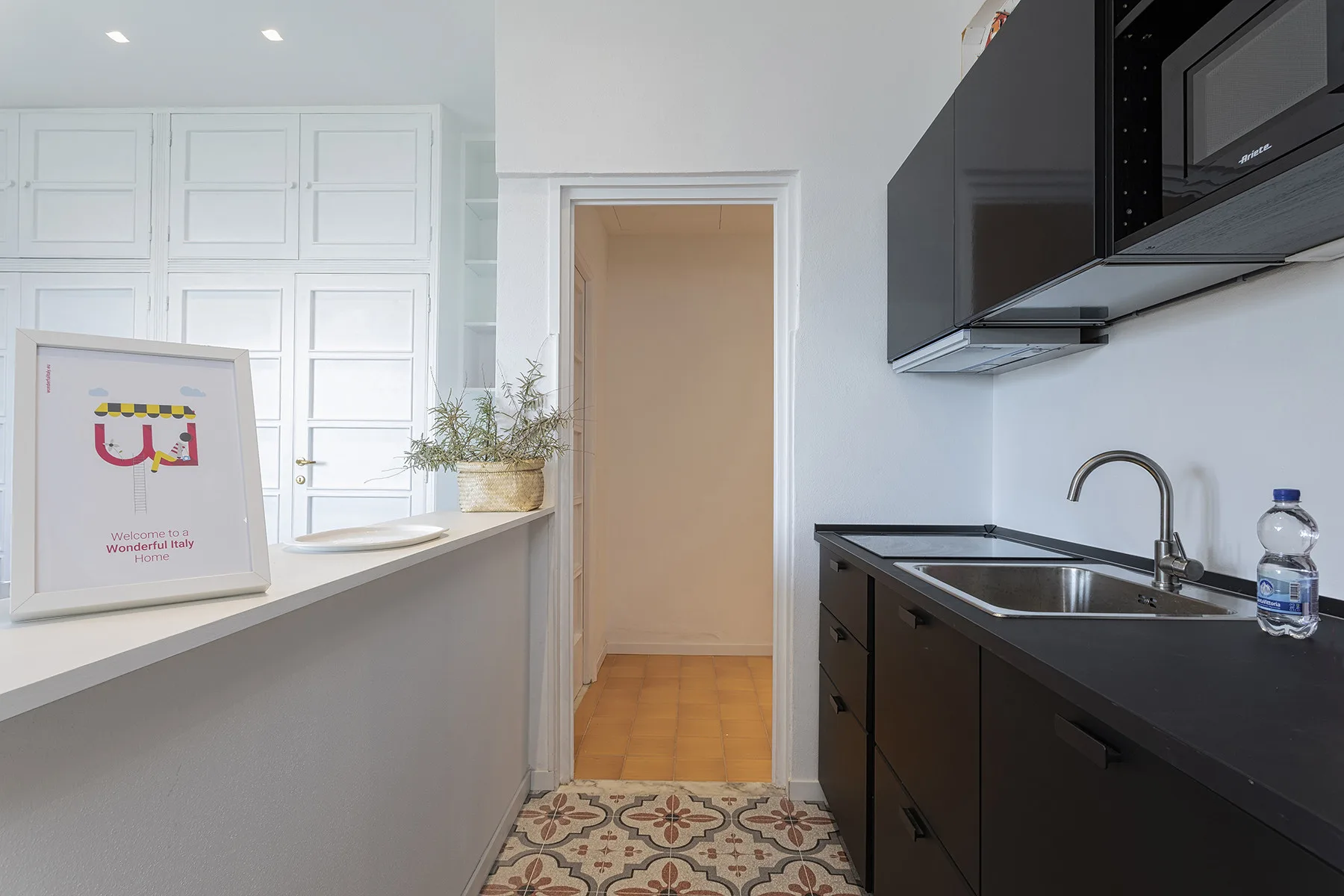 A compact kitchen with dark cabinets, a sink, and a counter opening onto a hallway.