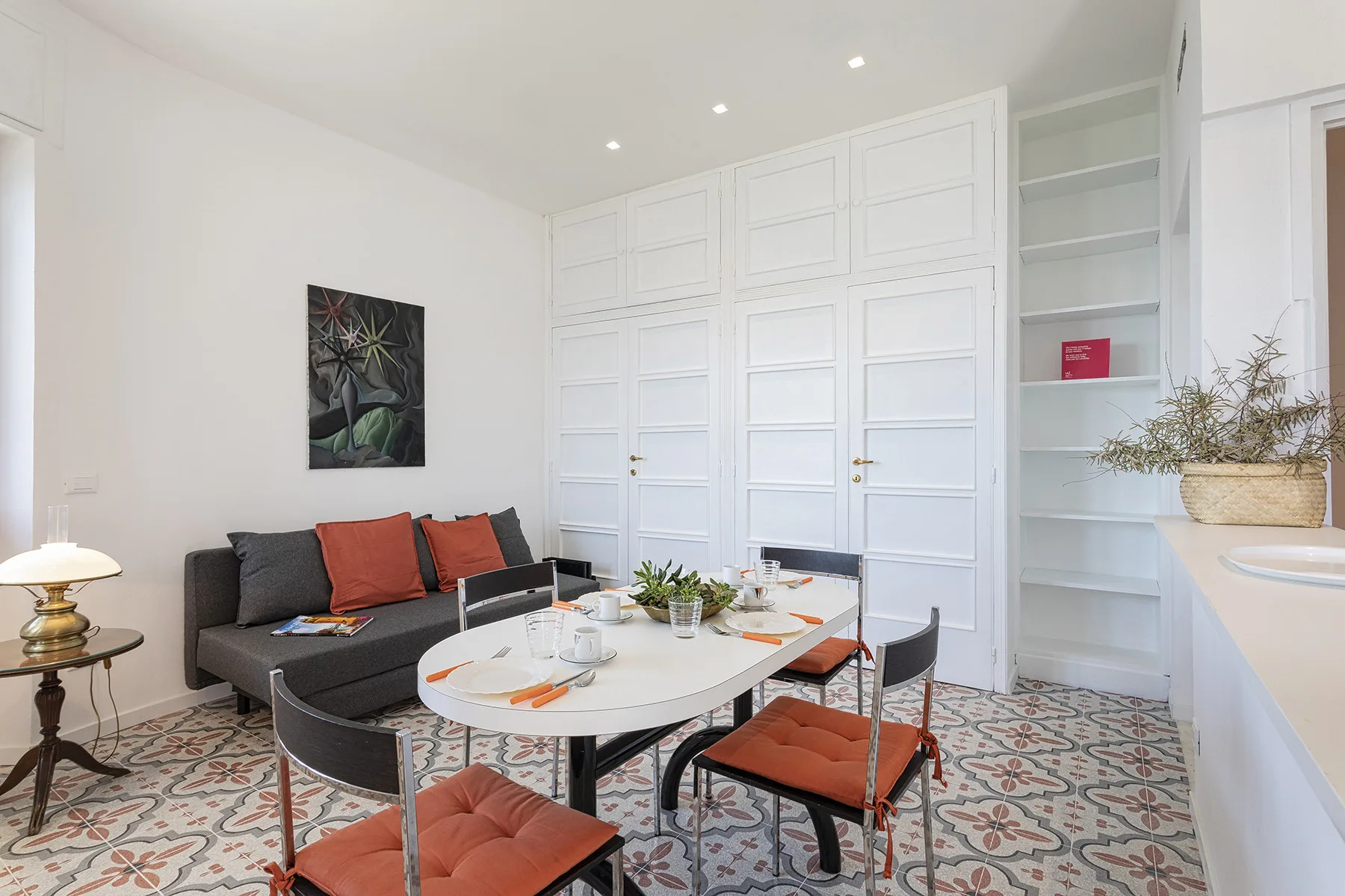 A bright dining area with a set table, gray seating, and white paneled doors.
