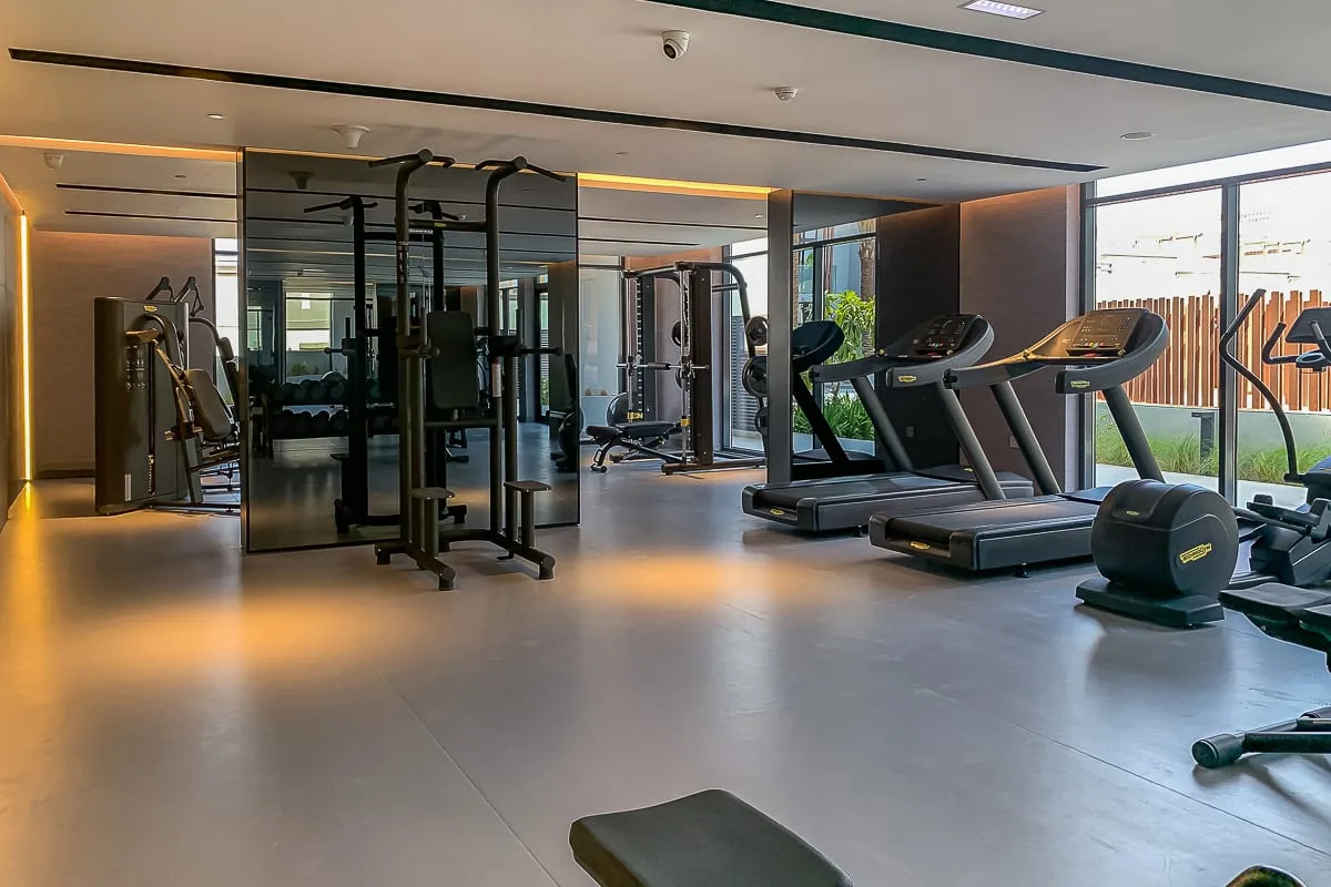 Un gimnasio con máquinas de ejercicio y cintas de correr junto a grandes ventanas.